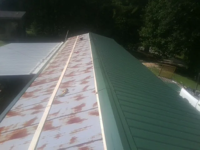 Old rusted panels beside newly installed green metal roofing — Wind Damage Roof Repair by Roofing Brothers in Cairnbrook
