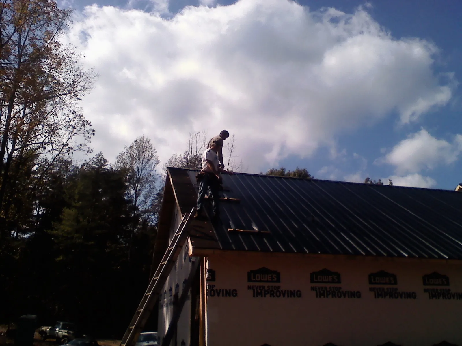Roofer fastening dark metal panels high against a cloudy sky, from a Roof Inspection job in Cairnbrook