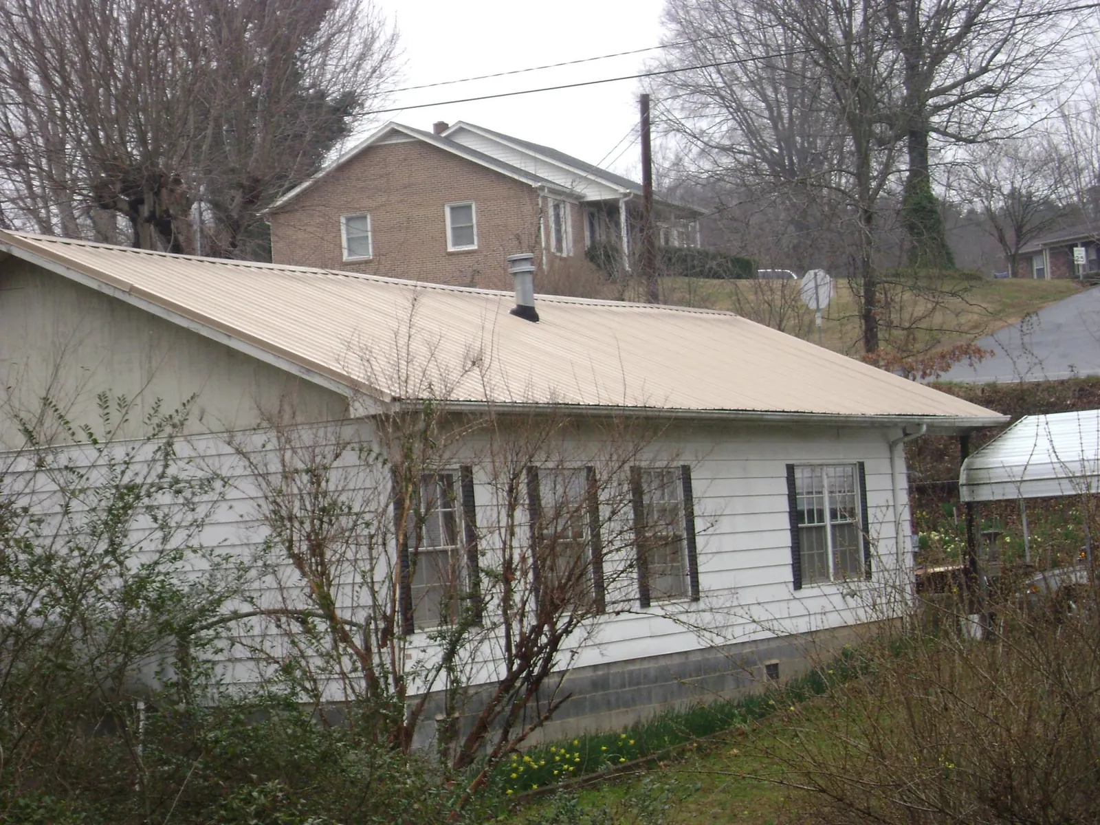Tan metal roof on a white sided house set into a hillside — Commercial Roofing by Roofing Brothers in Cairnbrook