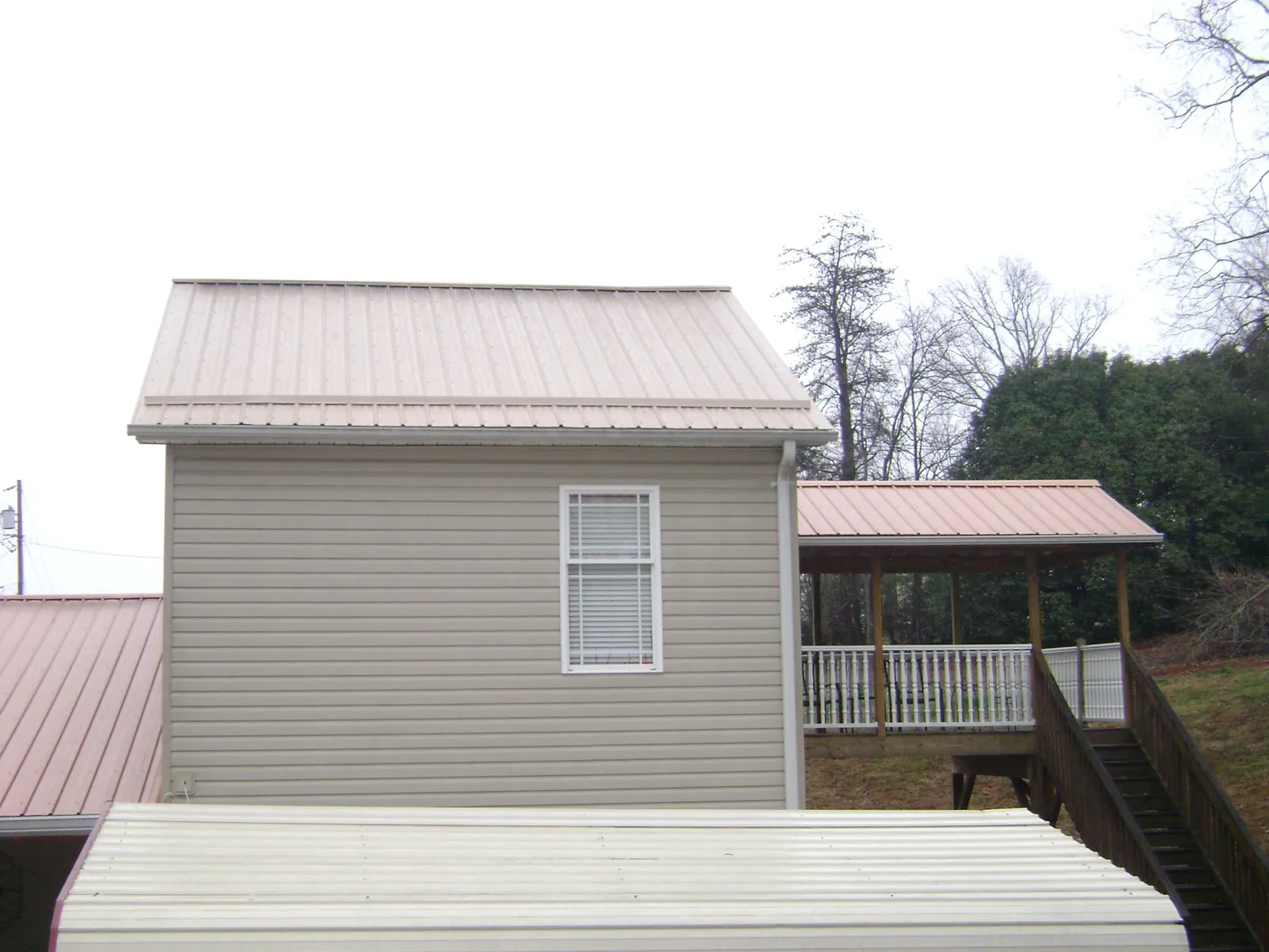 Tan metal roofs on a two story addition and attached porch, from a Roof Replacement job in Cairnbrook